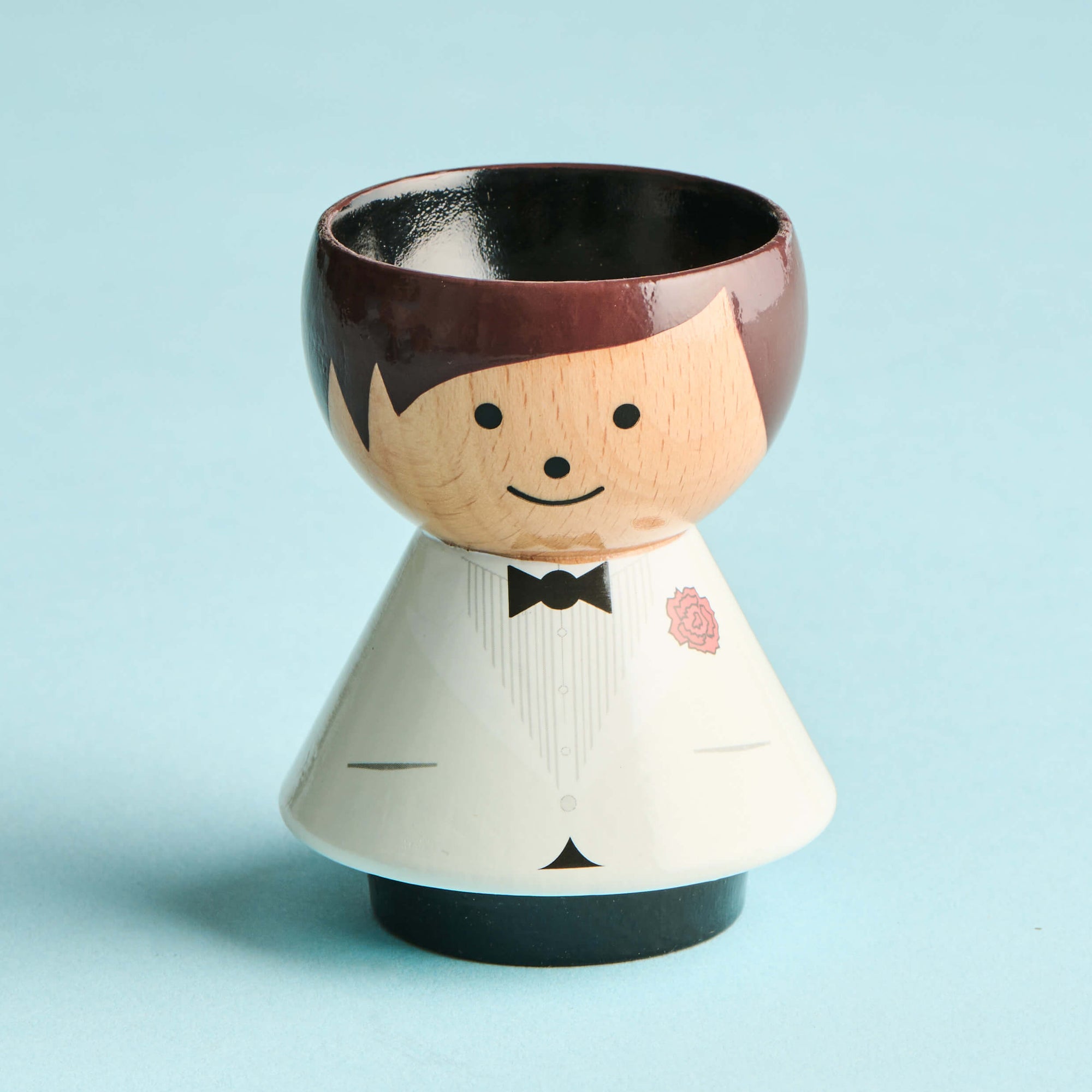 A wooden kokeshi doll with a tuxedo design and a bowl-shaped head on a light blue background.