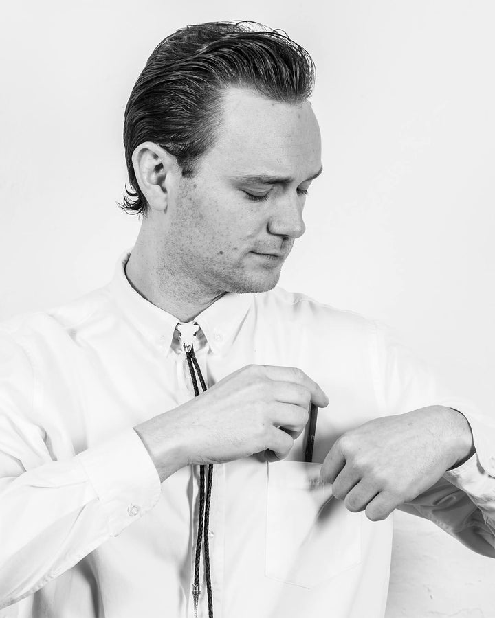 A person in a white shirt placing an item into their chest pocket, looking down.