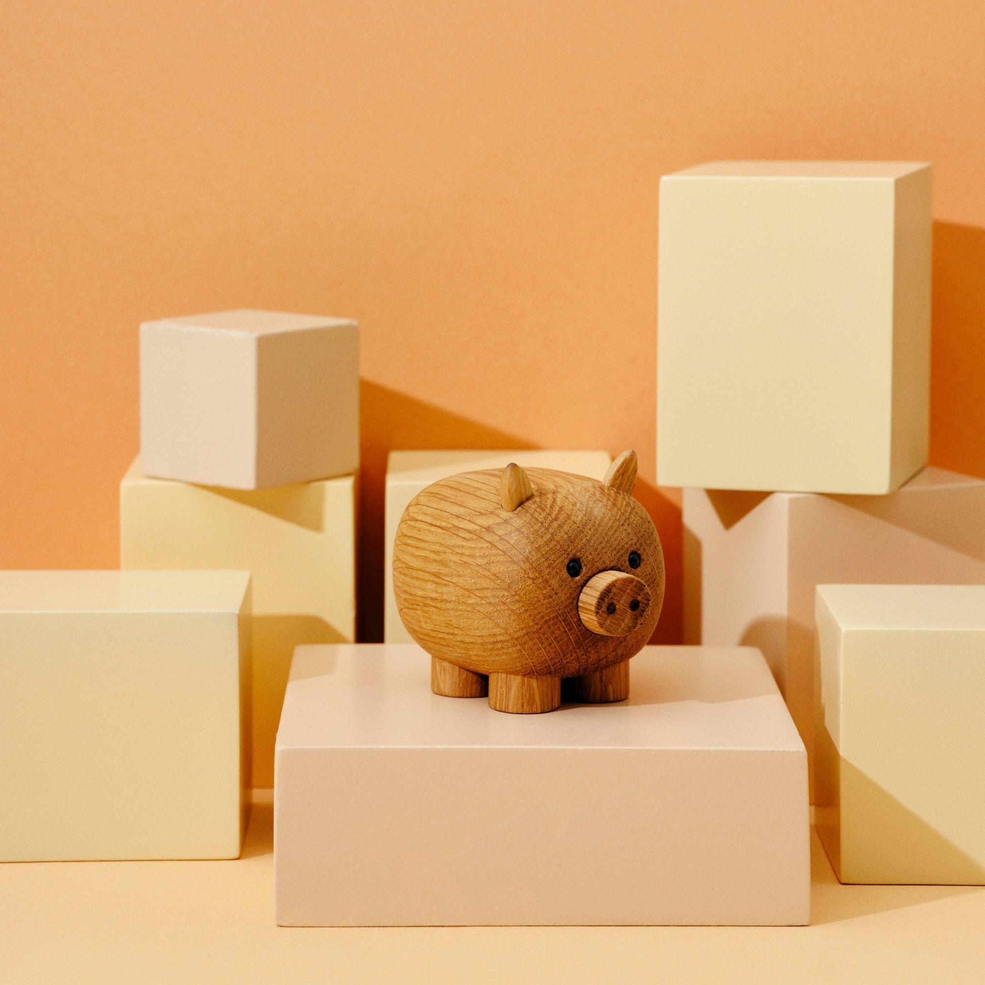 A wooden pig figurine on a display of beige and cream-colored geometric blocks.