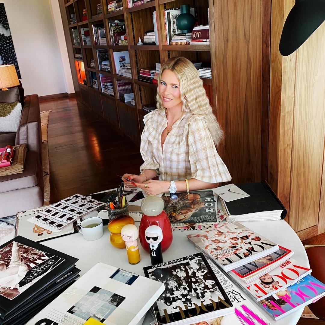 A person sitting at a table with magazines, kokeshi dolls, and decor items in a room with bookshelves.