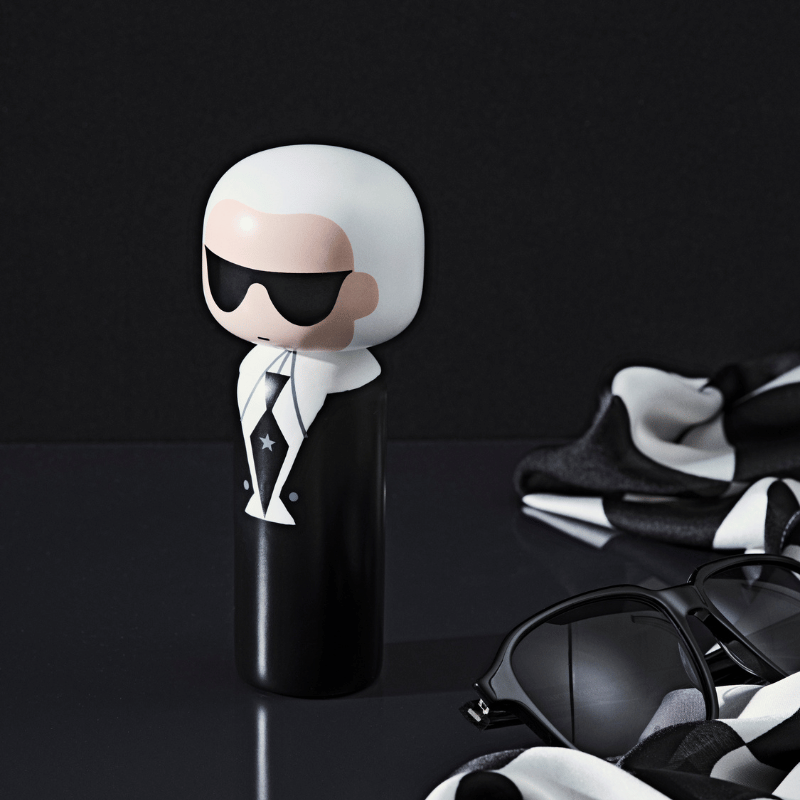 A kokeshi doll with sunglasses and a suit, next to a pair of sunglasses and a black-and-white scarf.