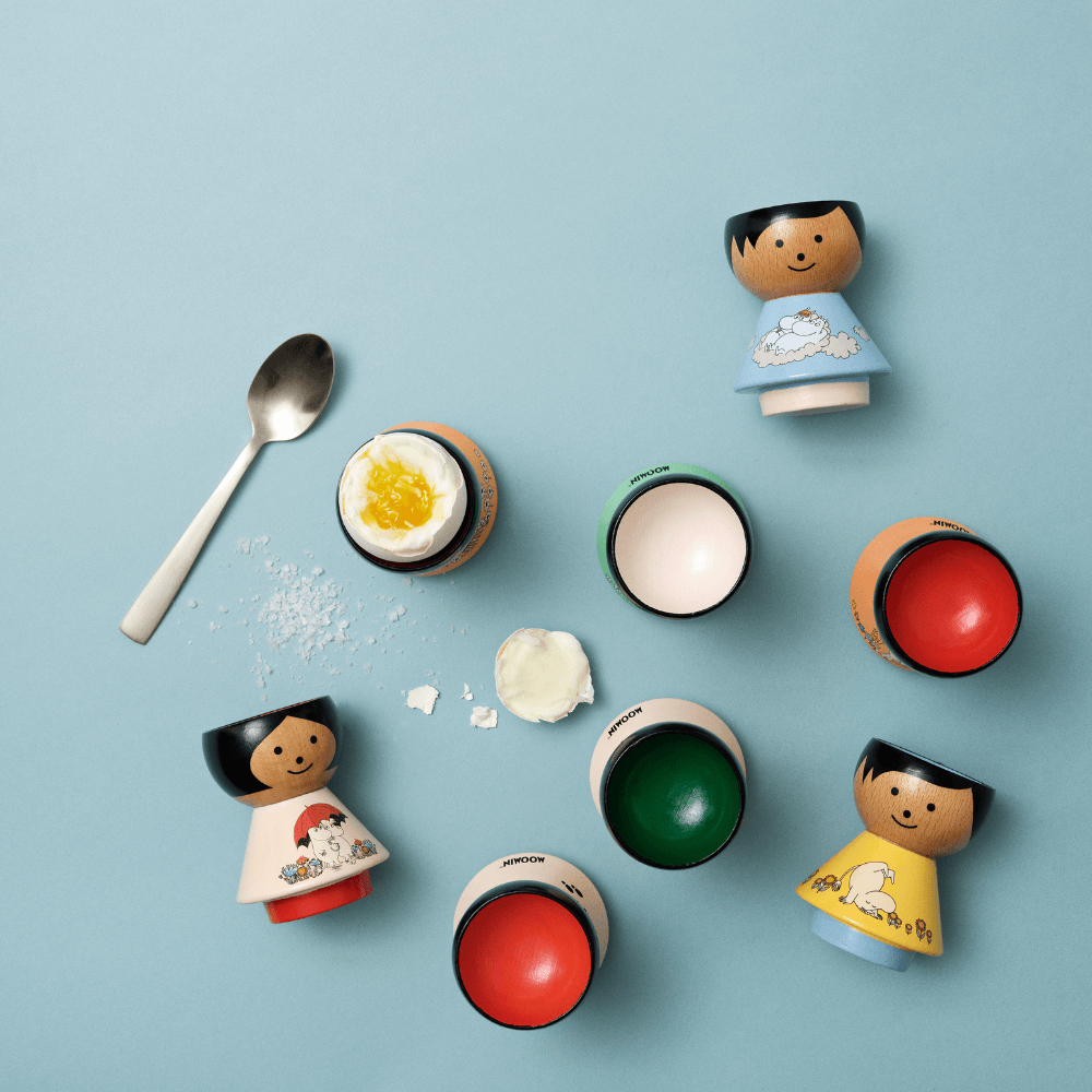 Kokeshi egg cups with various designs and a spoon on a blue background.