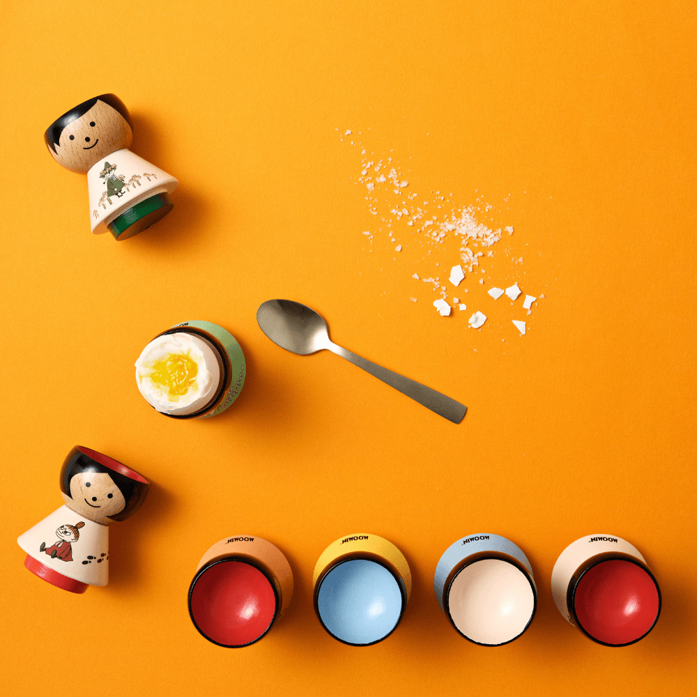 Kokeshi dolls, egg cups, a spoon, and salt on an orange background.