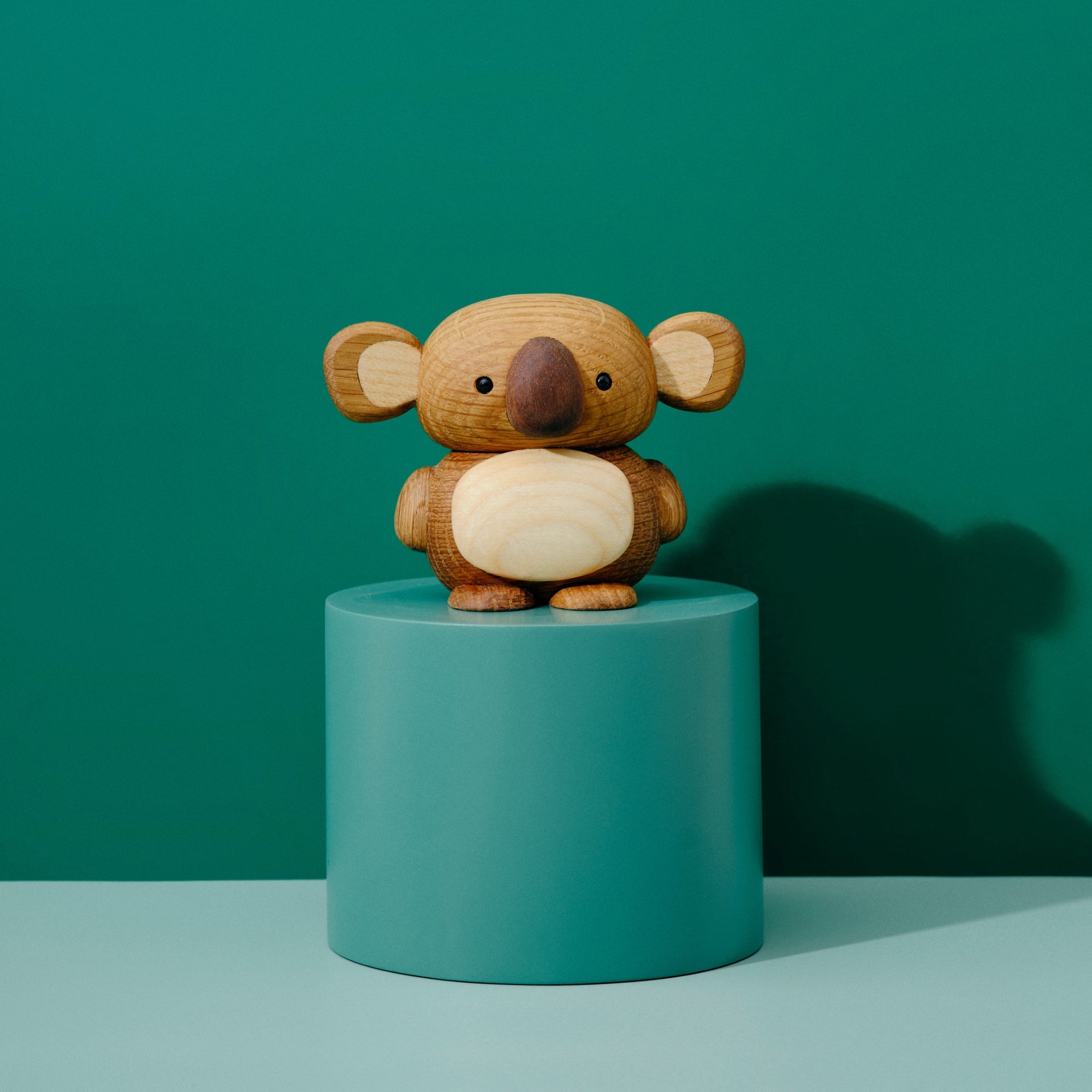 A wooden koala figurine on a teal pedestal against a matching teal background.