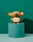 A wooden koala figurine on a teal pedestal against a matching teal background.