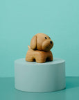 A small wooden dog figurine on a light blue cylindrical pedestal against a teal background.