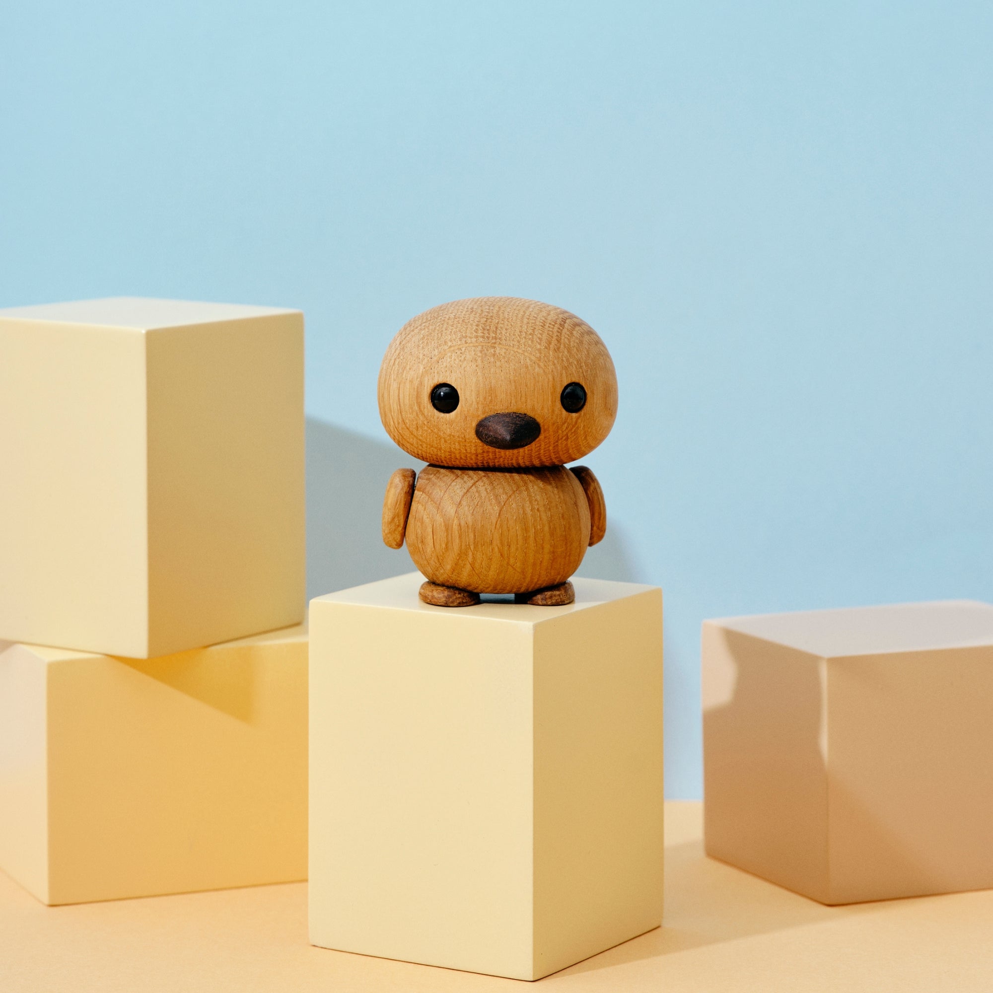 A small wooden bird figurine on pastel-colored blocks against a light blue background.