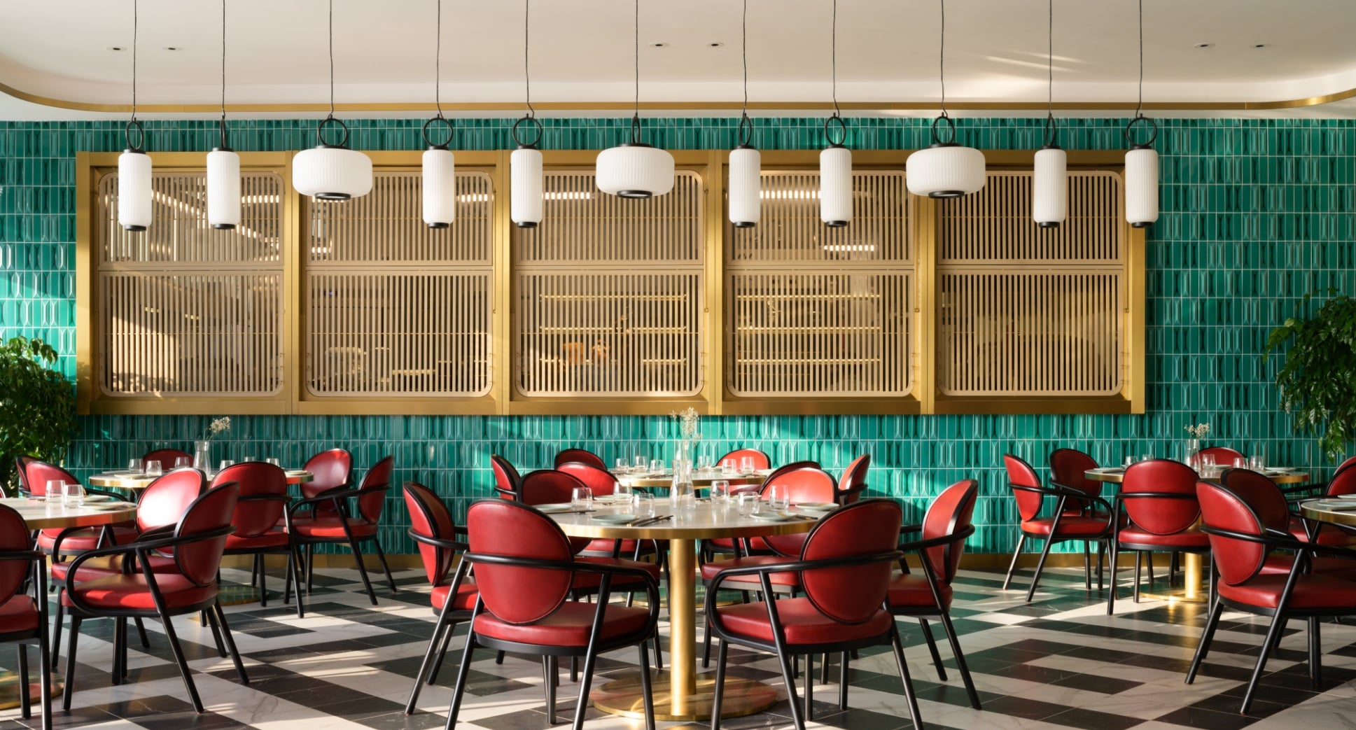 A restaurant interior with red chairs, green tiled walls, and white pendant lights.