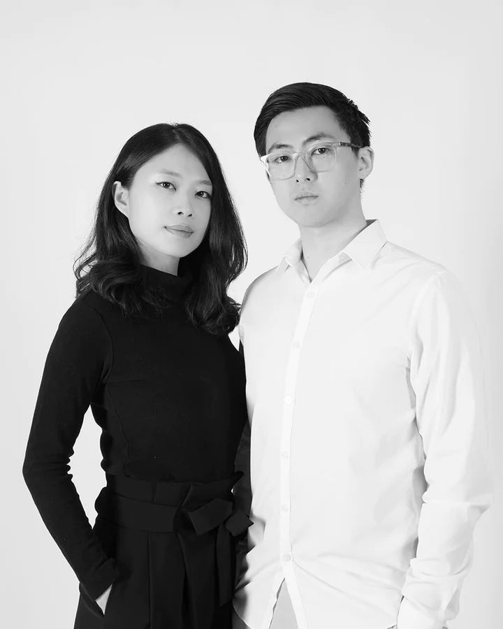 Two people standing side by side, one in a black outfit and the other in a white shirt, against a plain background.
