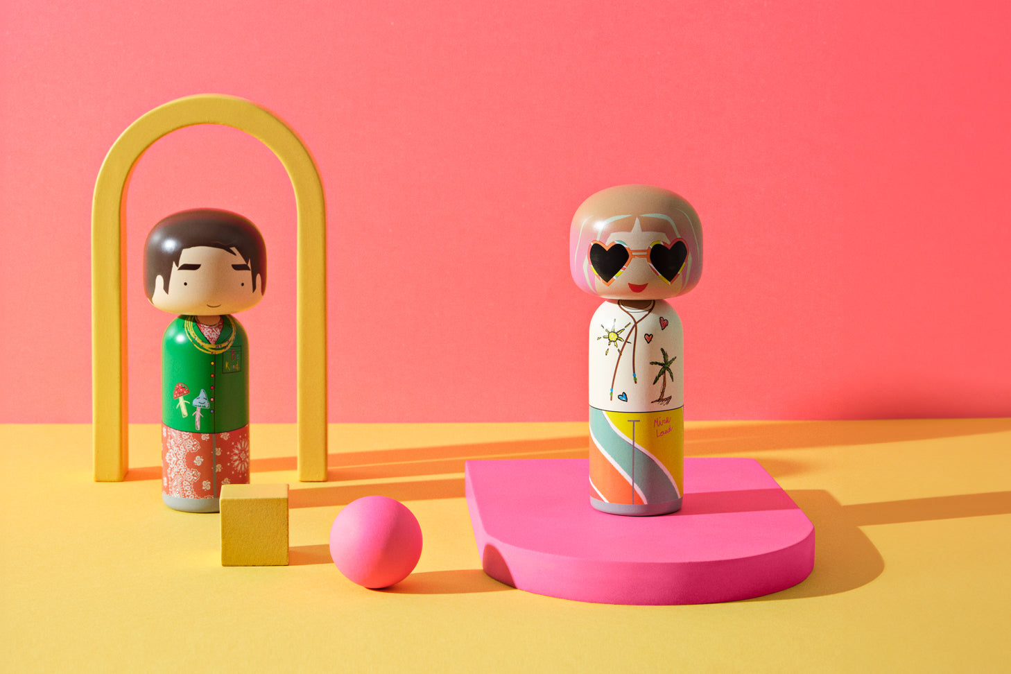 Two colorful kokeshi dolls on a vibrant pink and yellow background with geometric shapes.