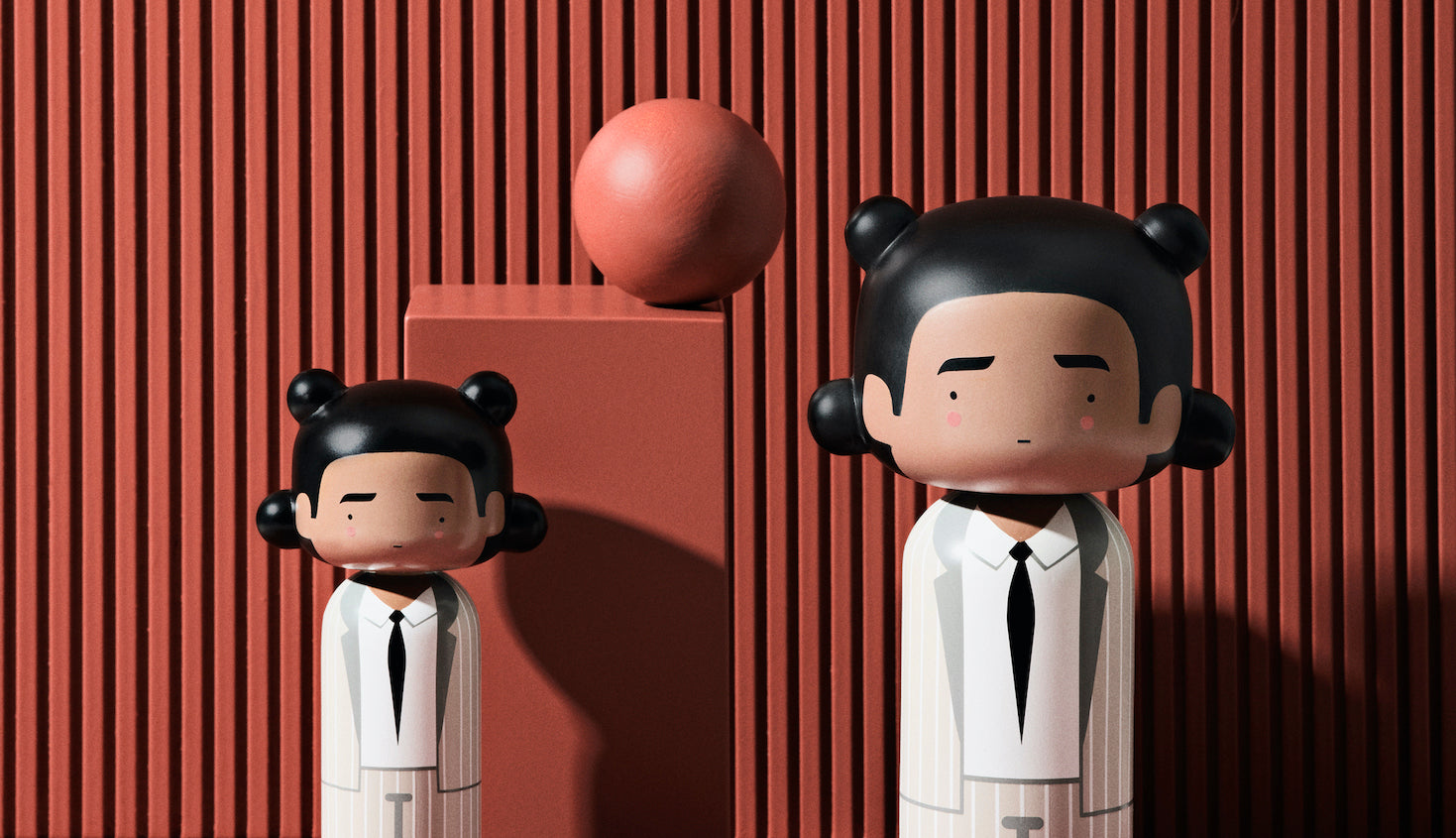 Two kokeshi dolls in white suits with black ties against a red striped background with a red sphere.