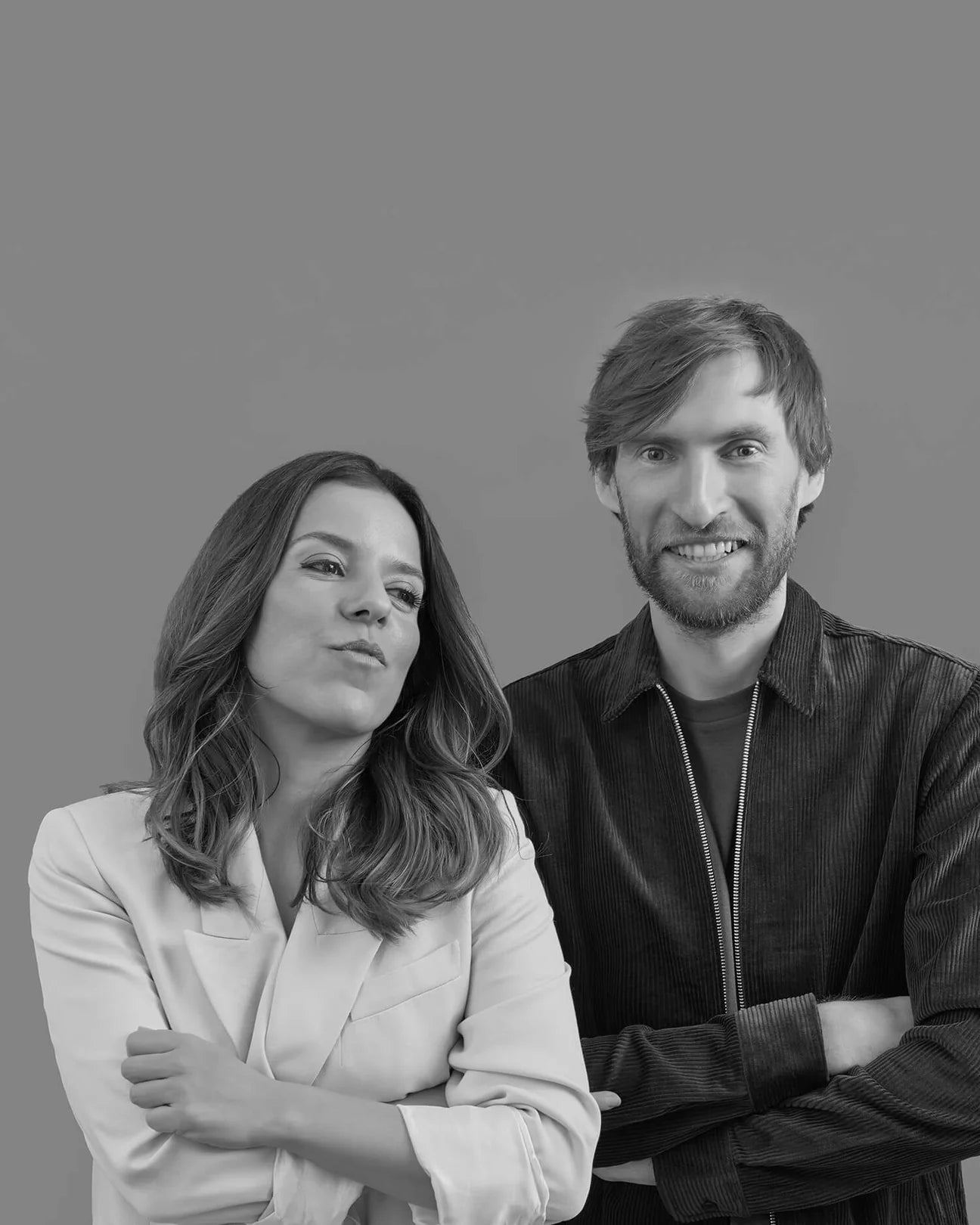 Two people standing side by side, both with arms crossed, smiling against a plain background.