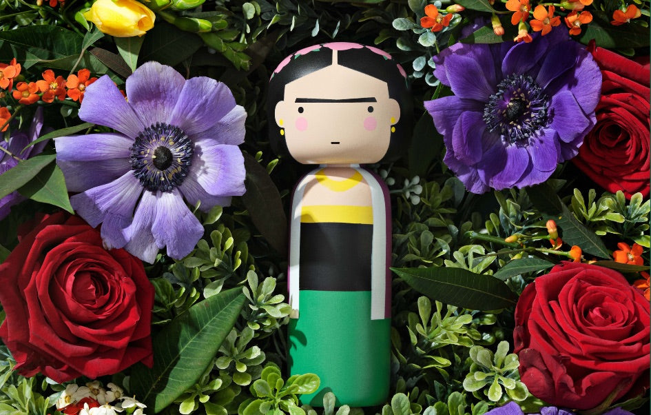 A kokeshi doll surrounded by vibrant flowers and greenery.