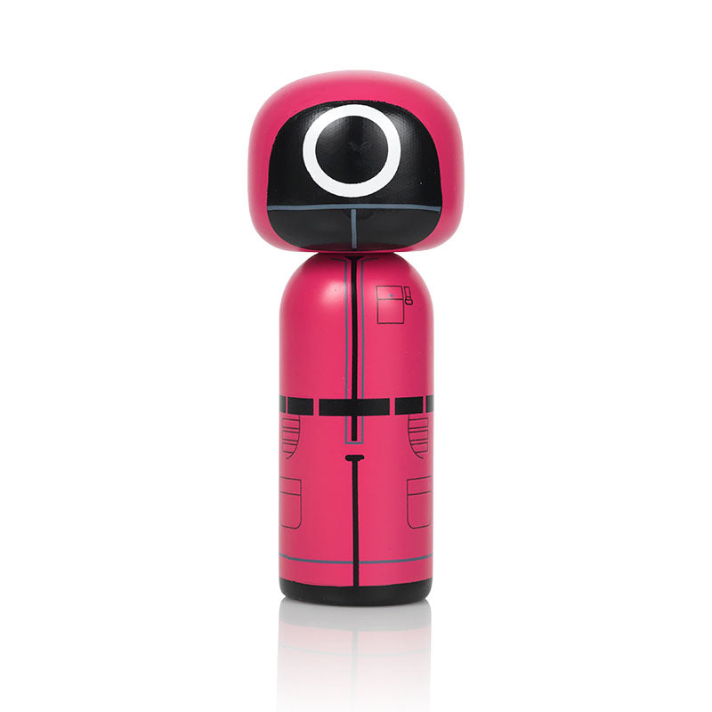 A pink kokeshi doll with a black and white circular face design, resembling a guard from a popular TV series.
