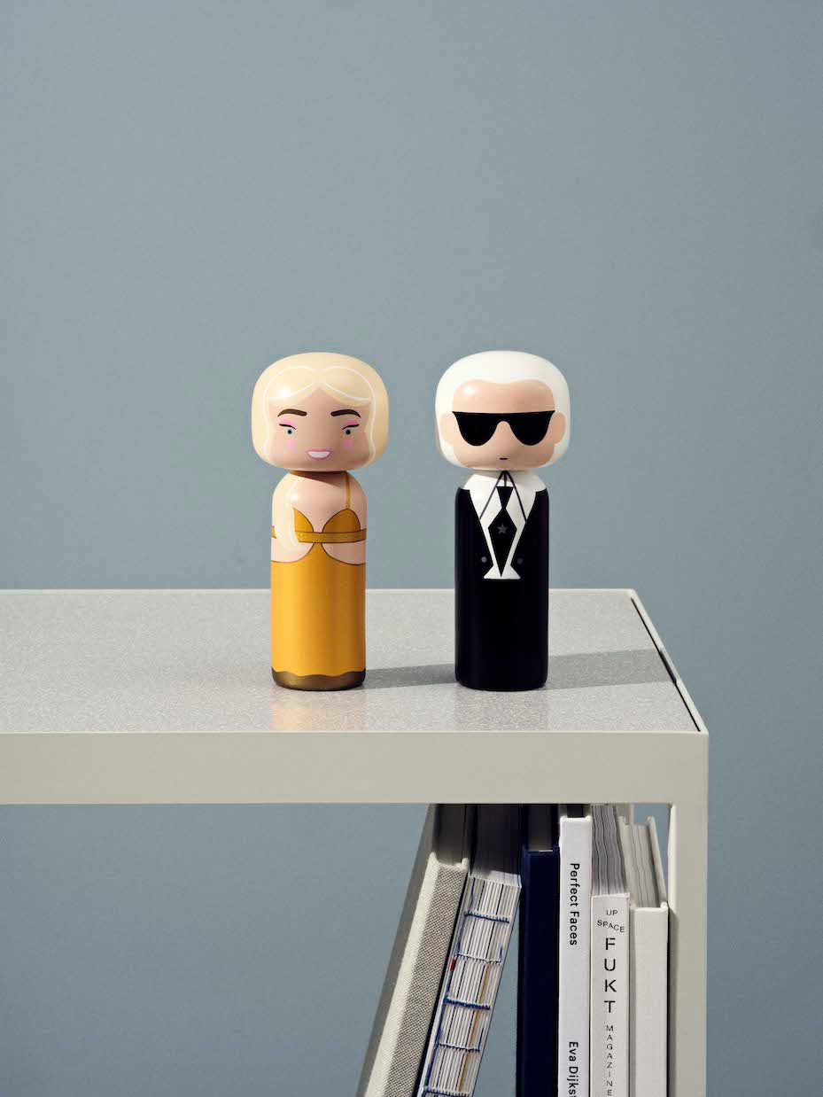 Two kokeshi dolls on a table, one in a yellow dress, the other in black with sunglasses.