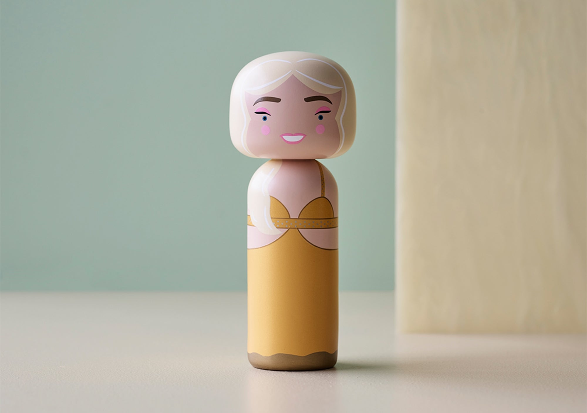 A kokeshi doll with a yellow dress and white hair on a light background.