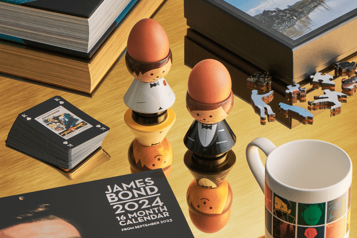 Kokeshi dolls dressed as a bride and groom on a table with books, a mug, a calendar, and puzzle pieces.