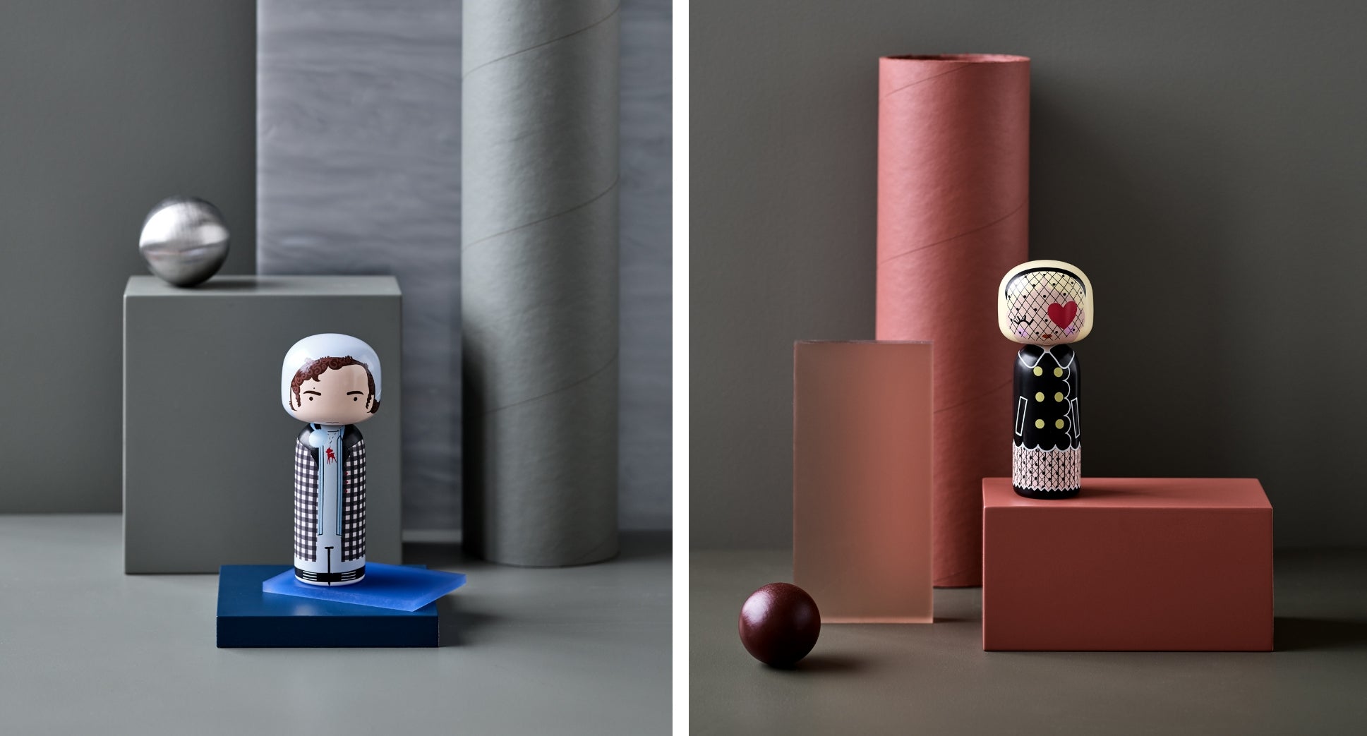 Two kokeshi dolls on geometric platforms with cylindrical and spherical decor in muted tones.