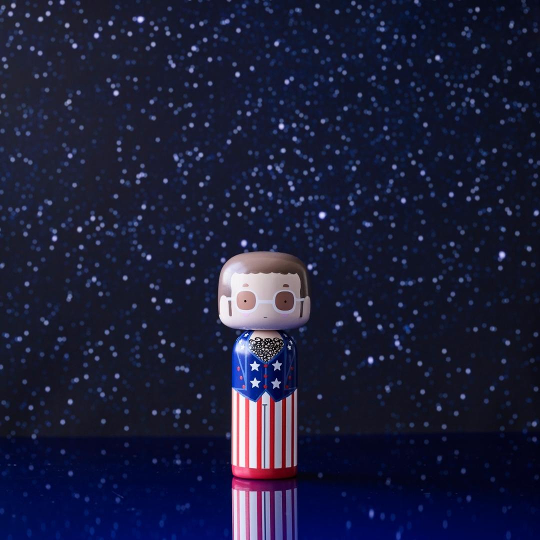En kokeshi-dukke med et patriotisk design står på en stjerneklar baggrund.