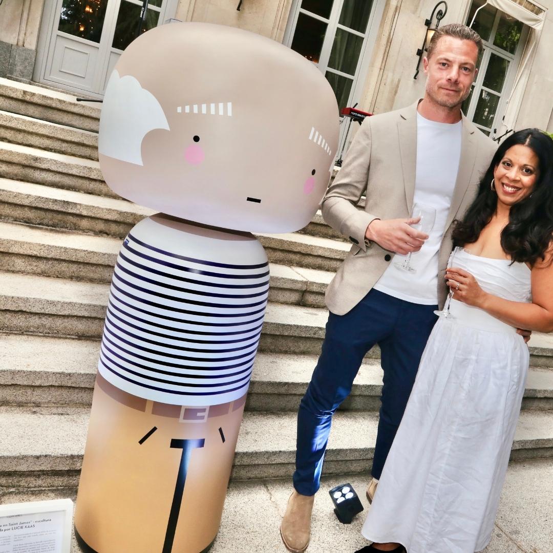 Et par poserer med en stor kokeshi-dukke på en stentrappe uden for en bygning.