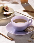 EnKop kaffe på en underkop med kiks, ved siden af en tallerken med ost og figner.