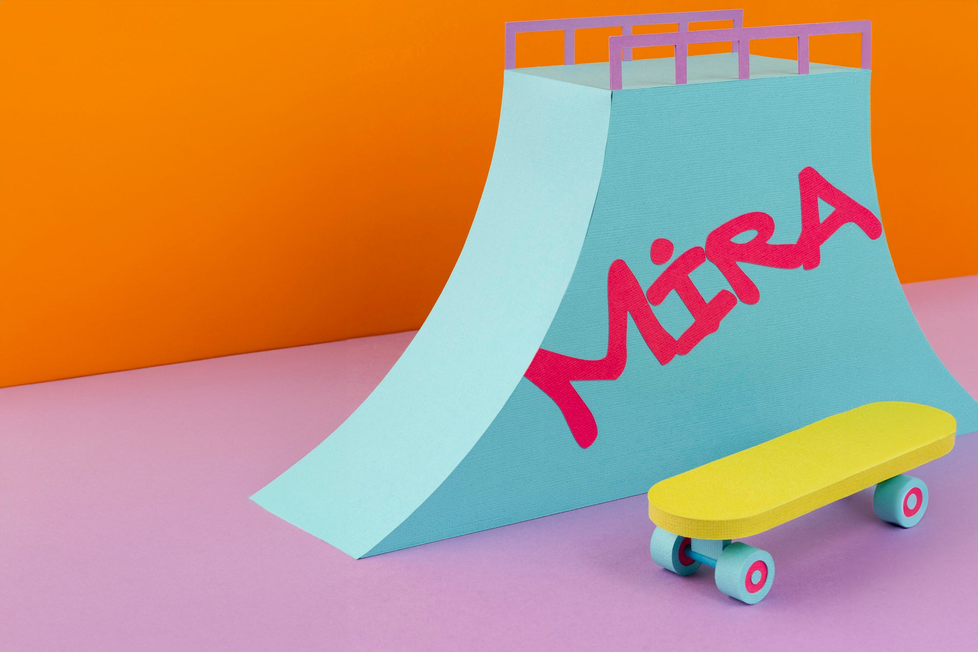 En farverig skateboardrampe med "Mira" skrevet på den og et gult skateboard foran.
