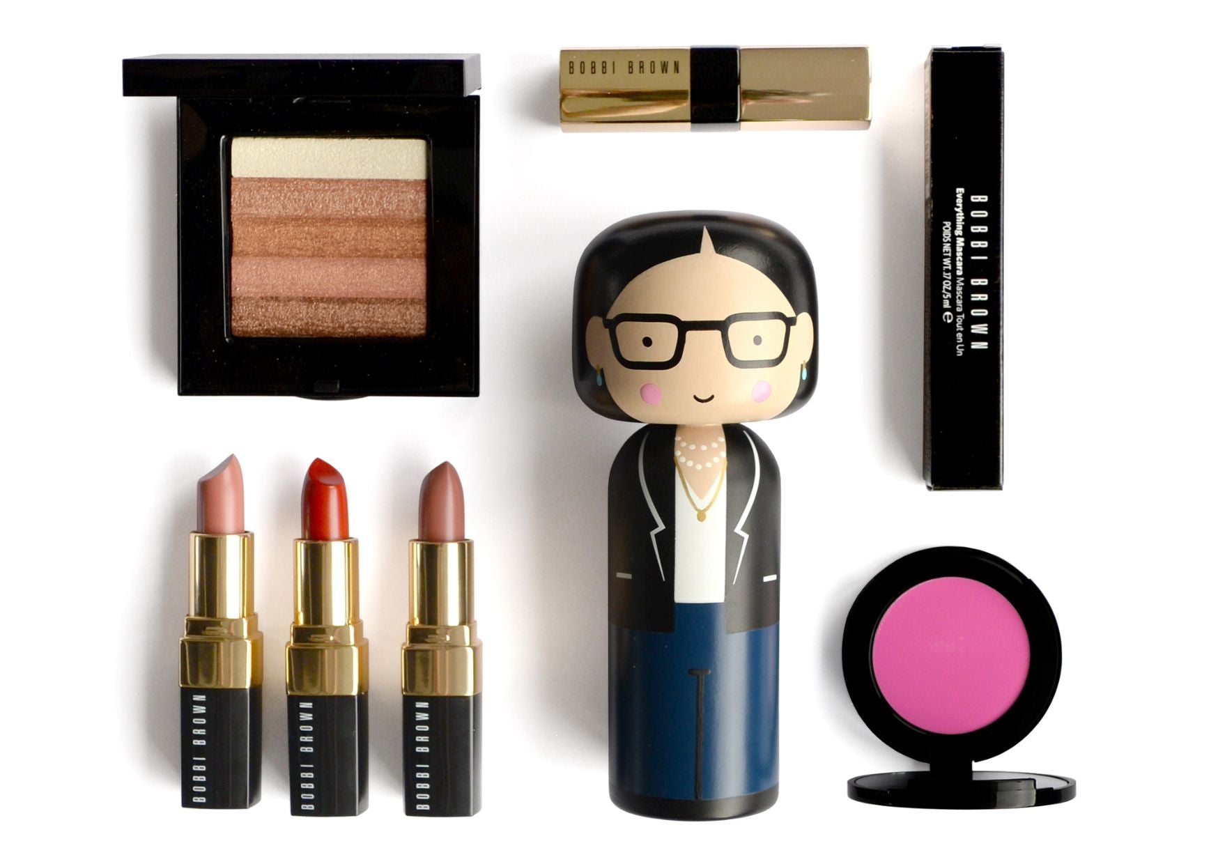 Kokeshi-dukke omgivet af makeup-artikler, bl.a. læbestifter, øjenskygge og blush.