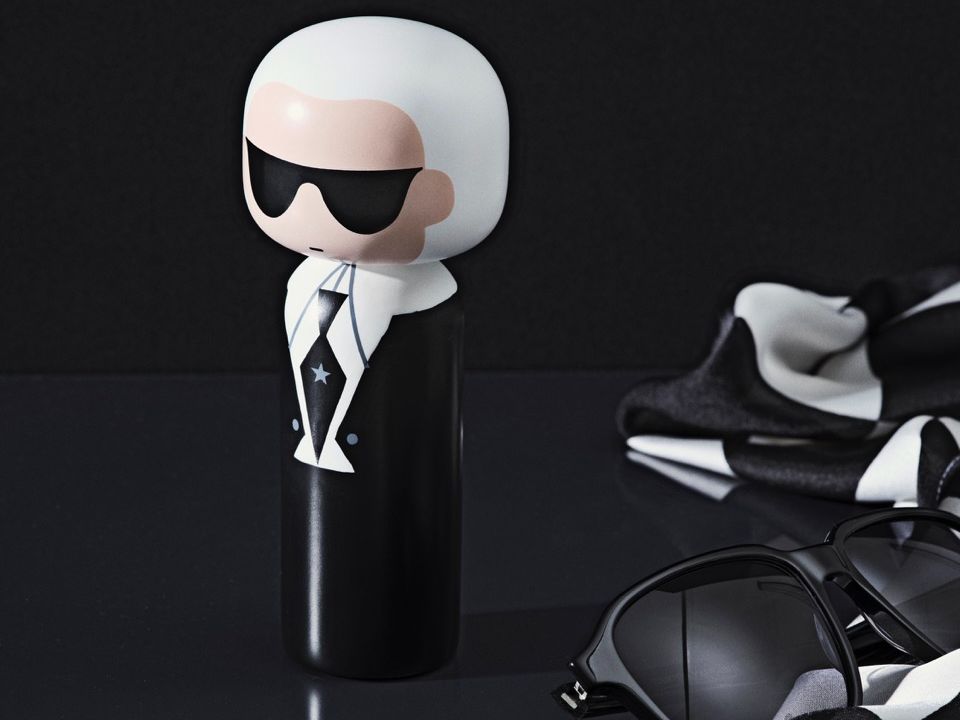 Kokeshi-Puppe mit Sonnenbrille und Anzug, daneben eine Sonnenbrille und ein Schal auf einer dunklen Fläche.