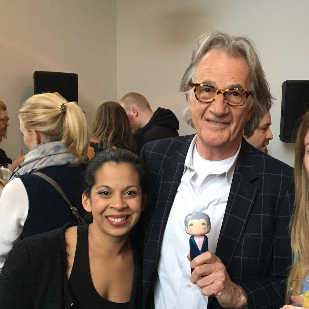 Eine Person, die eine Kokeshi-Puppe in der Hand hält, steht mit einer anderen Person bei einem Treffen in einem Gebäude.