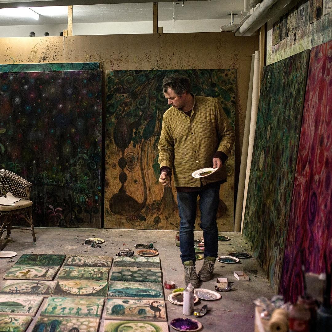 Künstlerin in einem Atelier, die auf Leinwänden malt, um die herum verschiedene Kunstwerke ausgestellt sind.