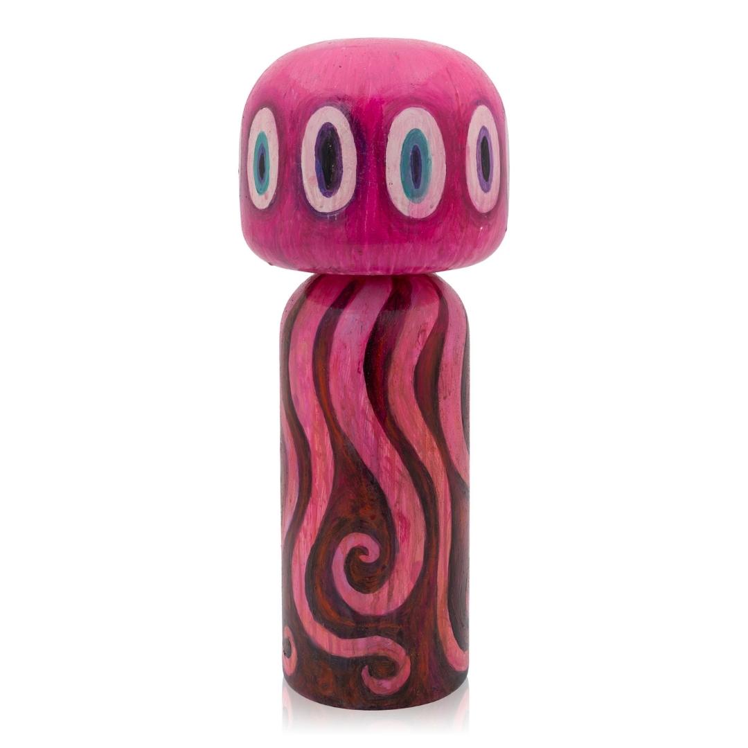 Eine rosa Kokeshi-Puppe mit mehreren Augen und tentakelartigen Mustern auf dem Körper.
