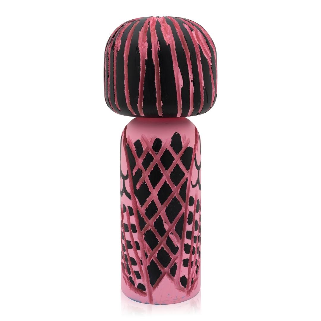Eine rosa-schwarze Kokeshi-Puppe mit abstrakten Mustern auf Körper und Kopf.