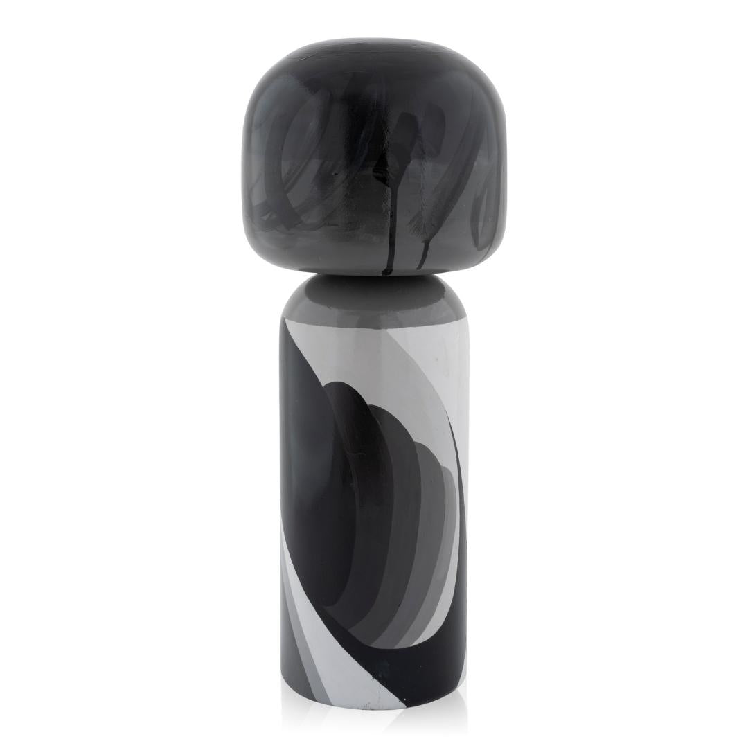 Schwarze und graue Kokeshi-Puppe mit abstrakten Mustern auf einem zylindrischen Sockel.