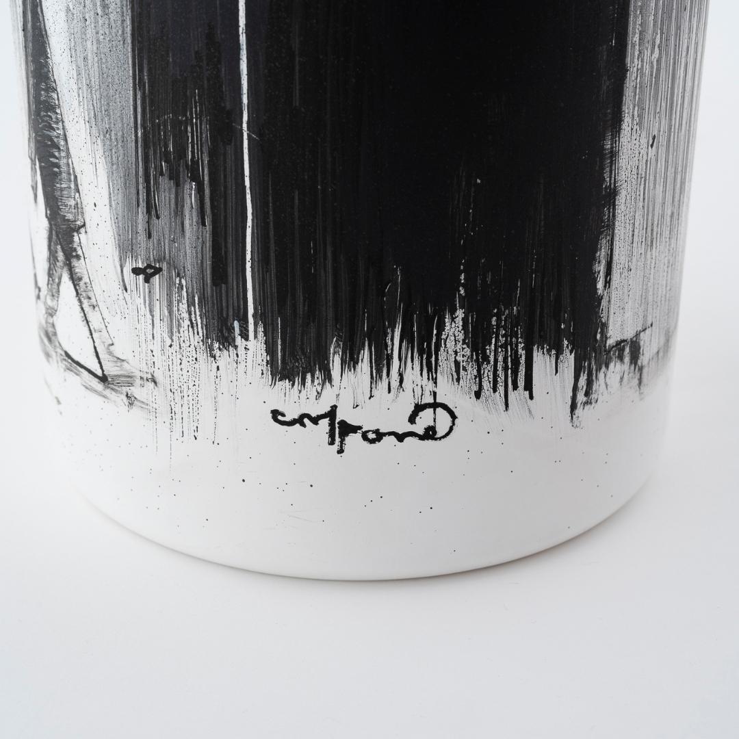 Schwarzes und weißes abstraktes Design auf einem zylindrischen Objekt mit einer Unterschrift am Boden.
