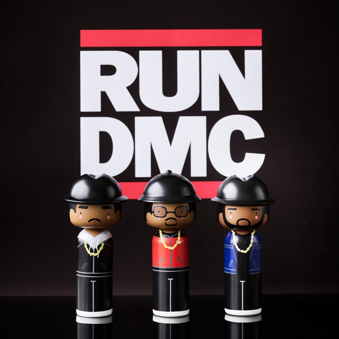Drei Kokeshi-Puppen, die Musikern ähneln, vor einem "RUN DMC"-Schild.