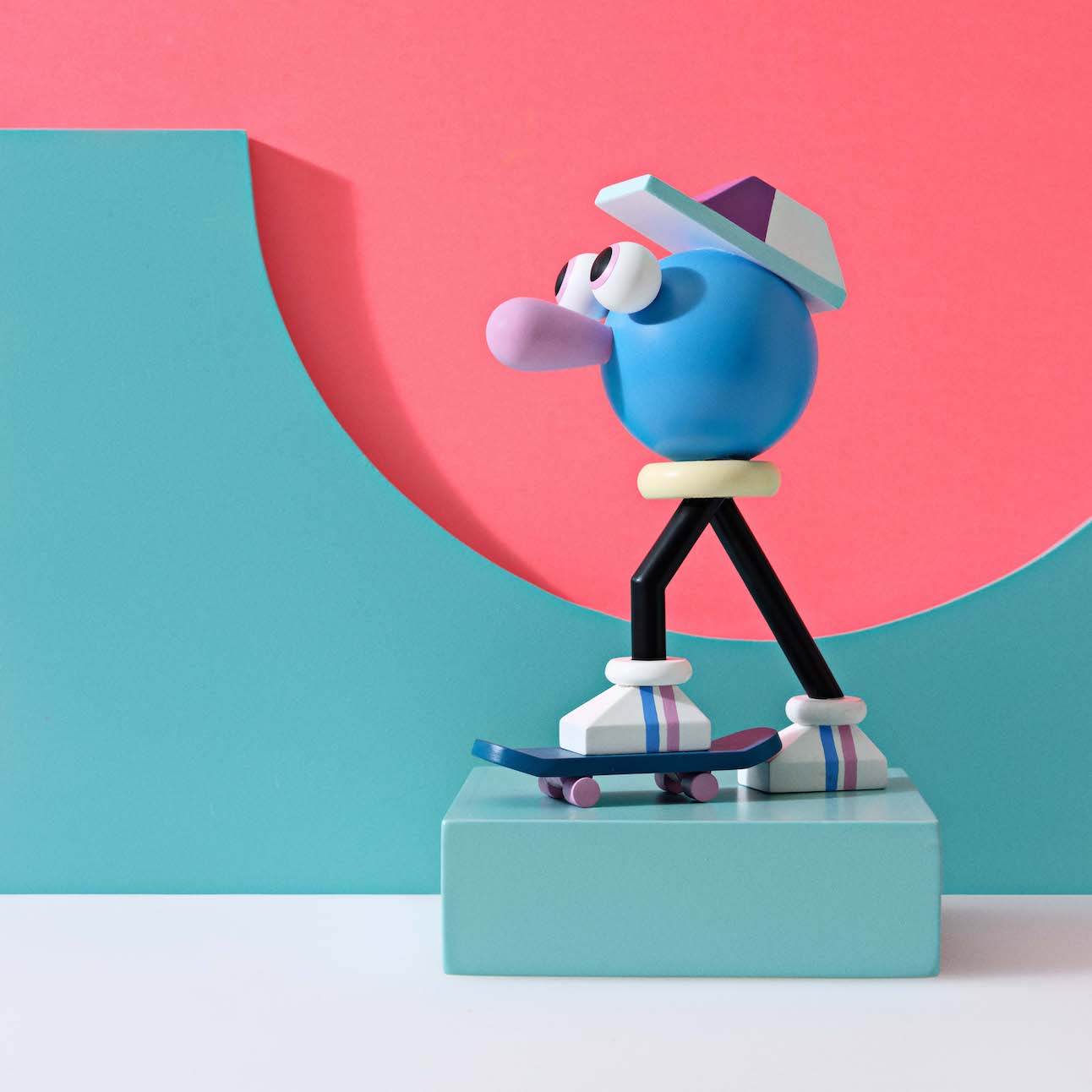 Eine farbenfrohe abstrakte Figur auf einem Skateboard vor einem geometrischen Hintergrund in Rosa und Grüntönen.