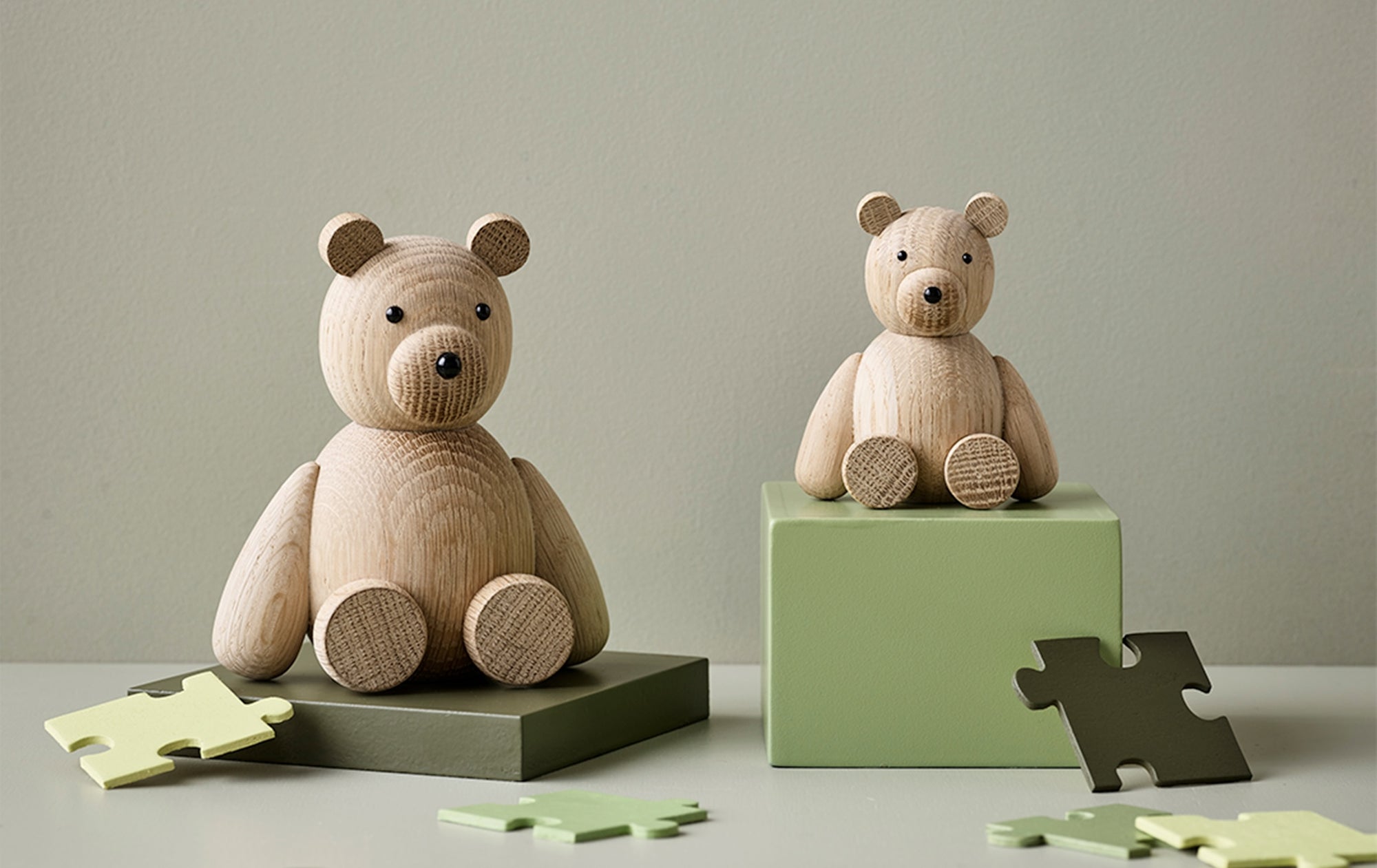 Hölzerne Bärenfiguren auf grünen Blöcken mit verstreuten Puzzleteilen.
