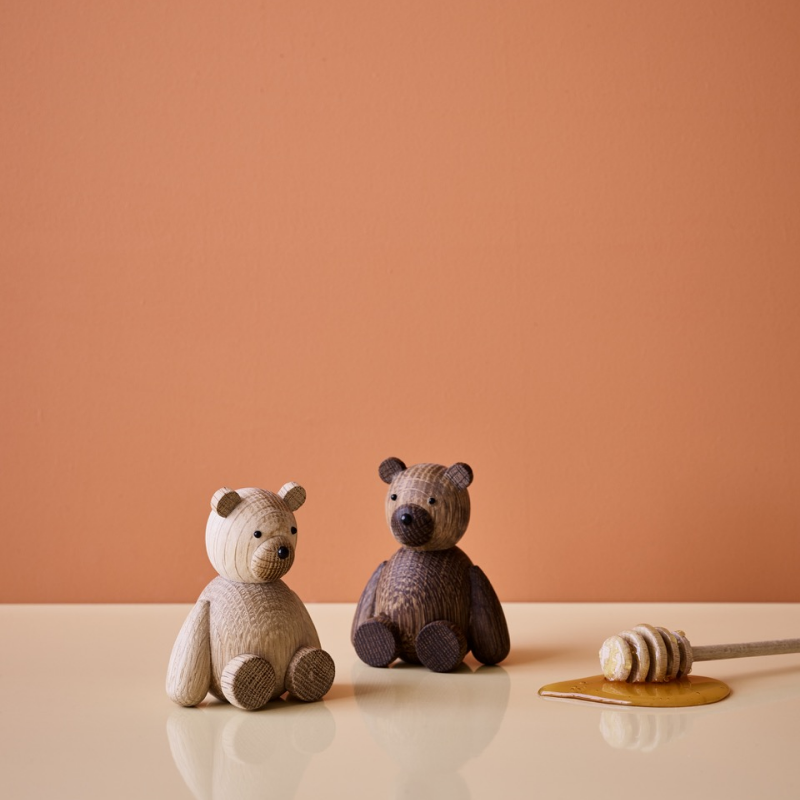 Zwei hölzerne Bärenfiguren sitzen auf einer beigen Fläche mit einem Honiglöffel und Honig in der Nähe.