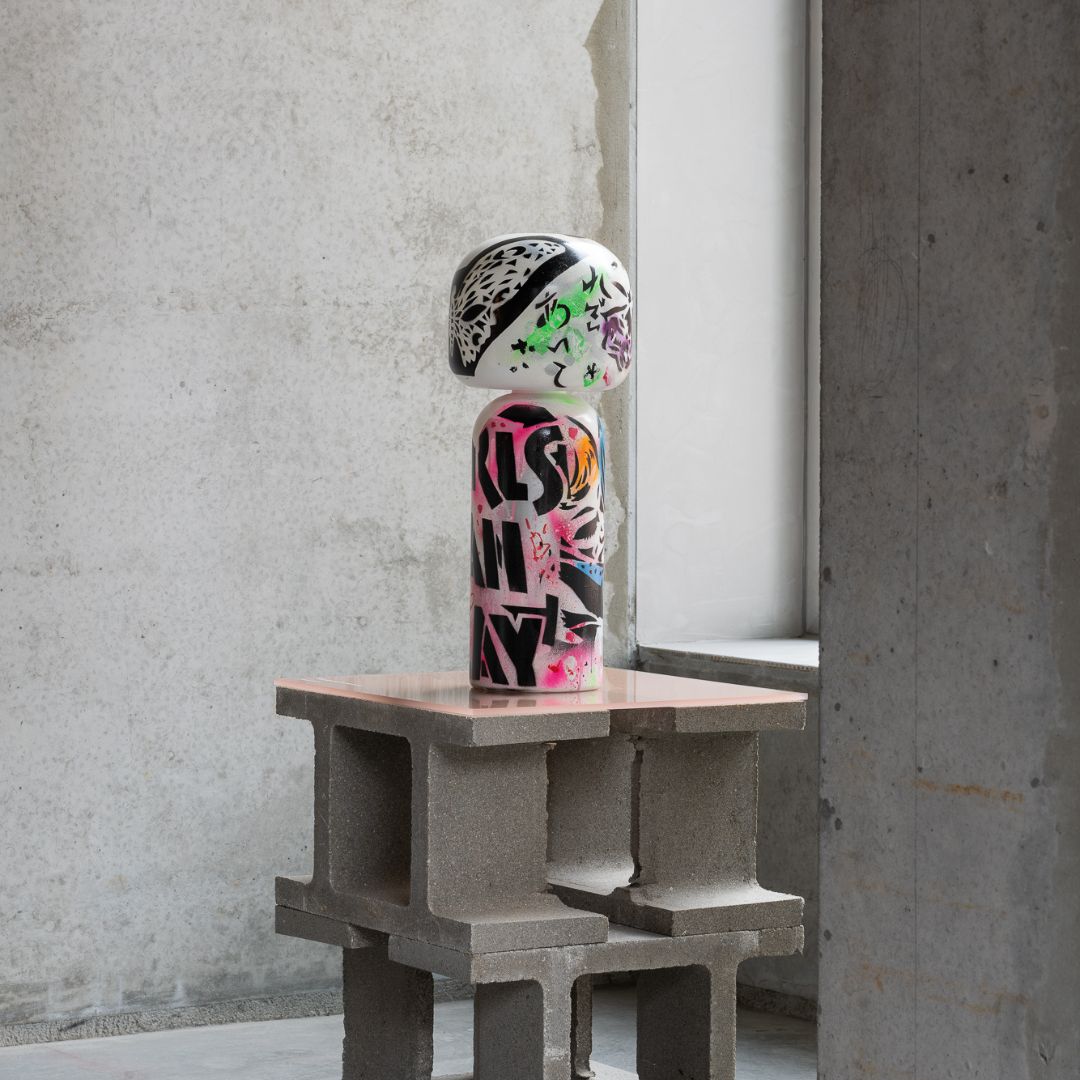Eine bunte Kokeshi-Puppe auf einem Tisch aus Betonblöcken in einem Raum im Industriestil.