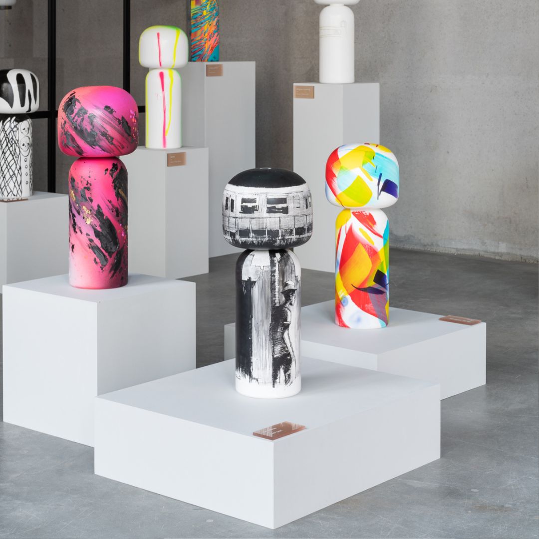 Bunte Kokeshi-Puppen auf weißen Sockeln in einer modernen, minimalistischen Umgebung.