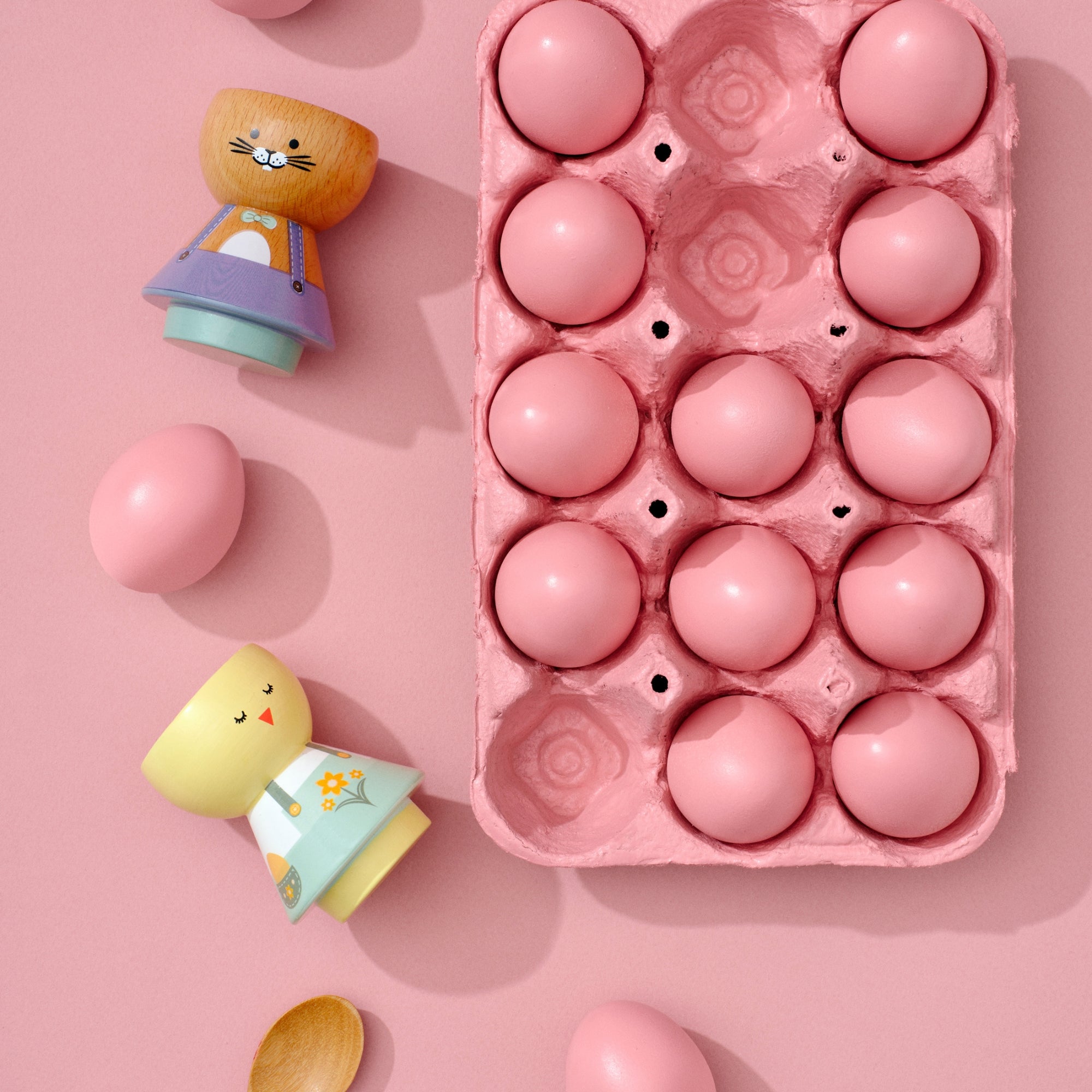 Poupées Kokeshi et œufs roses dans un carton sur fond rose.