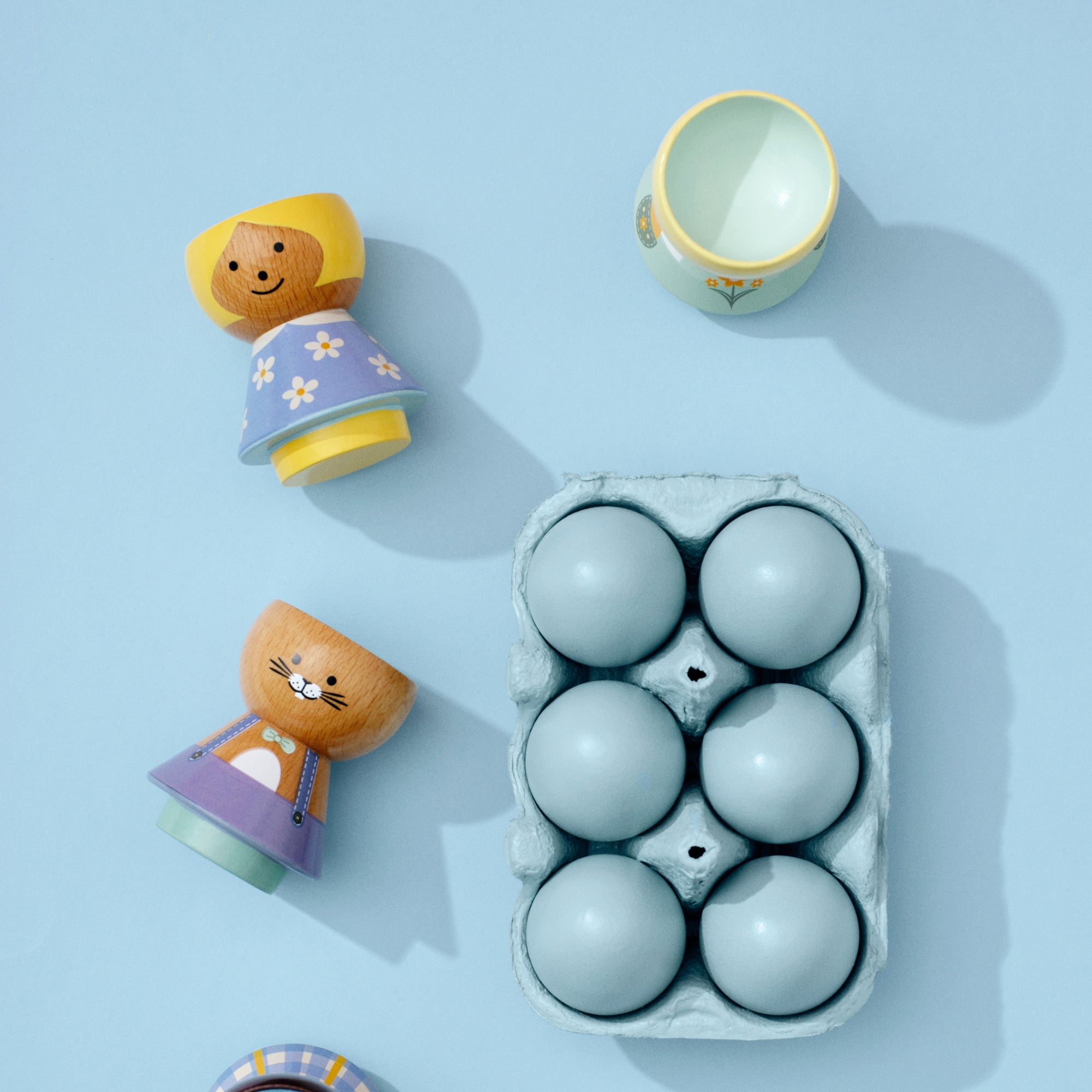 Pièces de poupée kokeshi en bois et carton d'œufs bleus sur fond bleu clair.