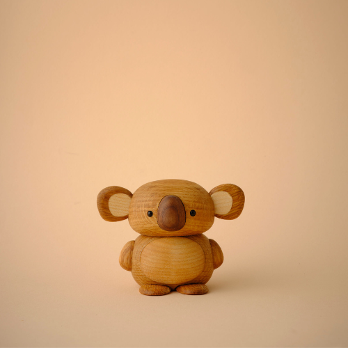 Petite figurine de koala en bois avec une finition lisse sur un fond beige uni.