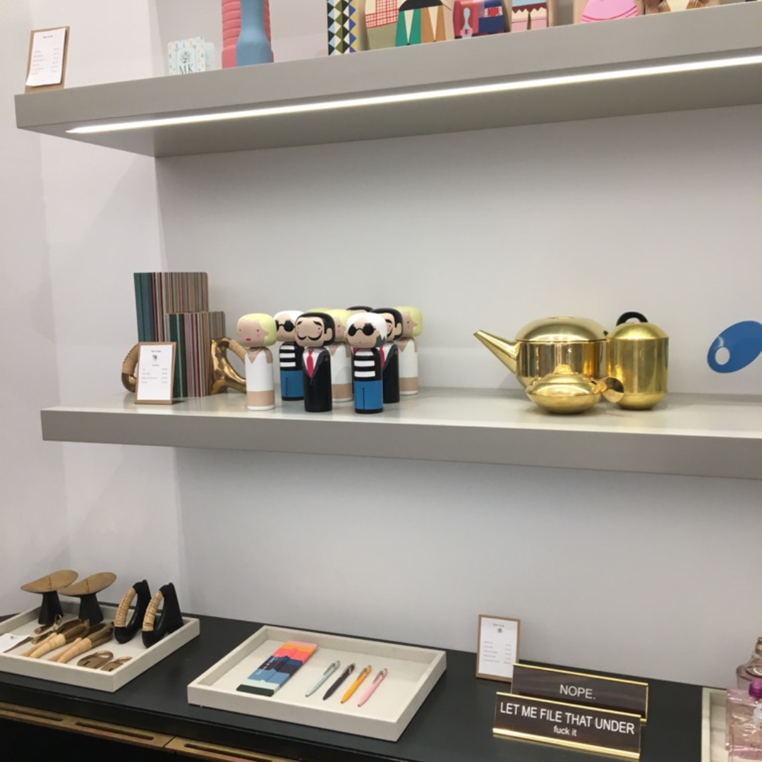 Présentoir d'étagère avec des poupées kokeshi, une théière en or et divers objets de décoration dans un magasin.