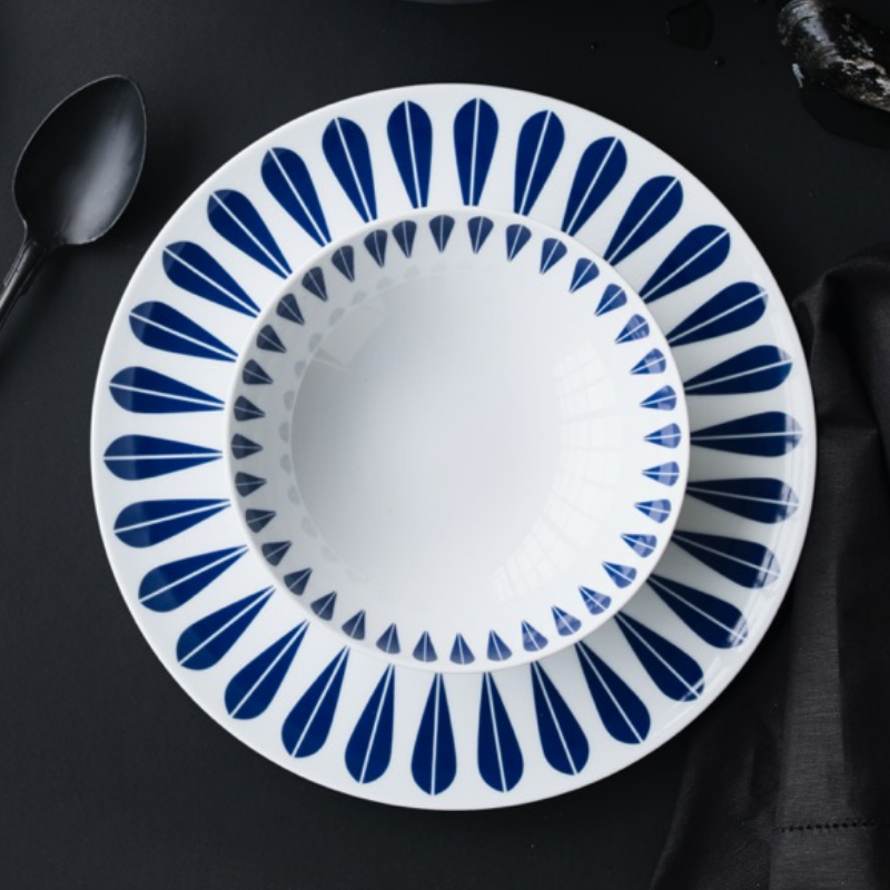 Assiettes blanches avec des motifs de feuilles bleues sur une surface foncée, accompagnées d'une cuillère et d'une serviette.