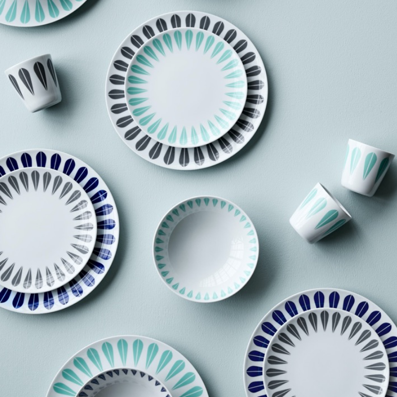 Assiettes et tasses blanches avec des motifs de pétales sarcelle, noir et marine sur une surface bleu clair.
