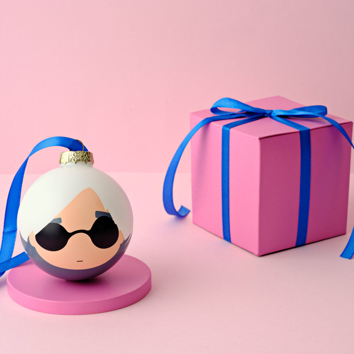 A decorative ornament with sunglasses next to a pink gift box with a blue ribbon.