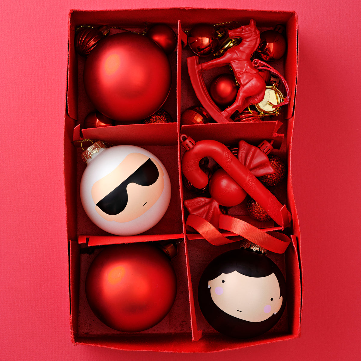 A red box with assorted red and white Christmas ornaments, including kokeshi doll designs.