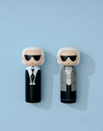 Deux poupées kokeshi avec des lunettes de soleil et des tenues élégantes sur un fond bleu clair.