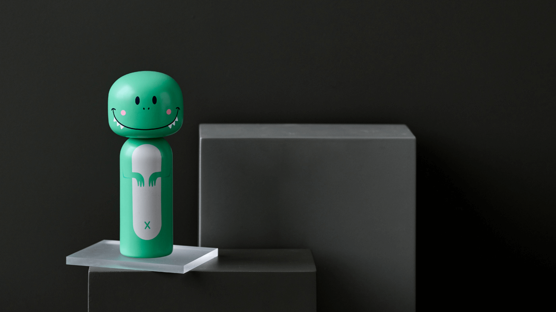 Une poupée kokeshi verte avec un visage souriant sur un fond noir et gris minimaliste.
